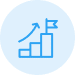 Blue icon of three ascending steps with an upward arrow and a flag at the top, symbolizing growth, progress, or achievement, on a light blue circular background.